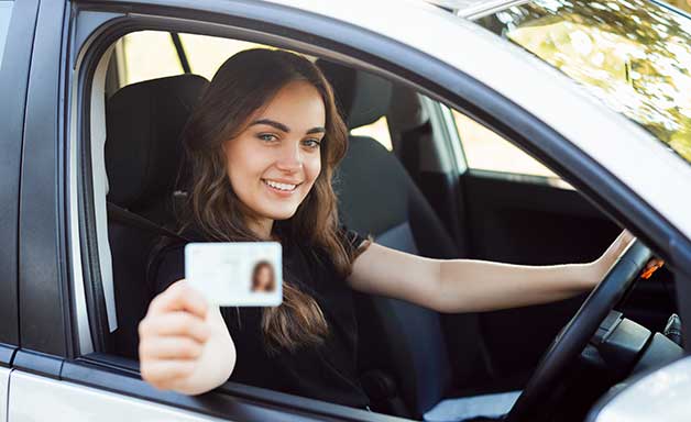 Happy driver sitting in the modern silver car and showing driving car license 